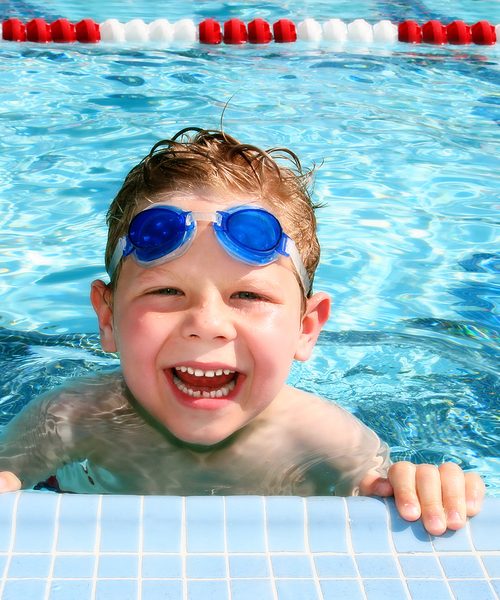 Smiling six year old boy in a sunny swimming pool